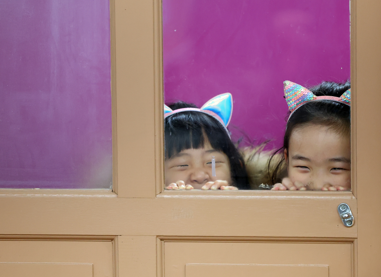 Soon-to-be elementary school students are seen peaking through a window into their classroom at an elementary school in Busan on Wednesday. (Yonhap)