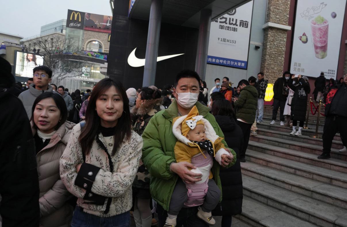A man carries a child at a shopping mall in Beijing, Dec. 30,2023. China's population dropped by 2 million people in 2023 in the second straight annual drop as births fell and deaths jumped (AP Photo/Ng Han Guan)