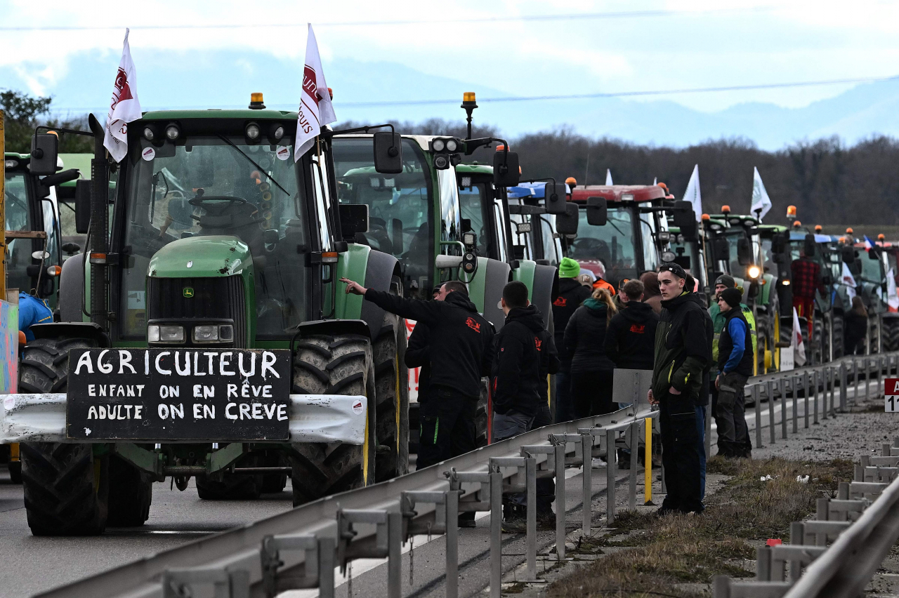 French farmers stand next to their tractors as they block the road, during a demonstration at the French-German border in Ottmarshe, eastern France, on Friday, as part of nationwide protests called by several farmers' unions over pay, tax and regulations. (AFP)