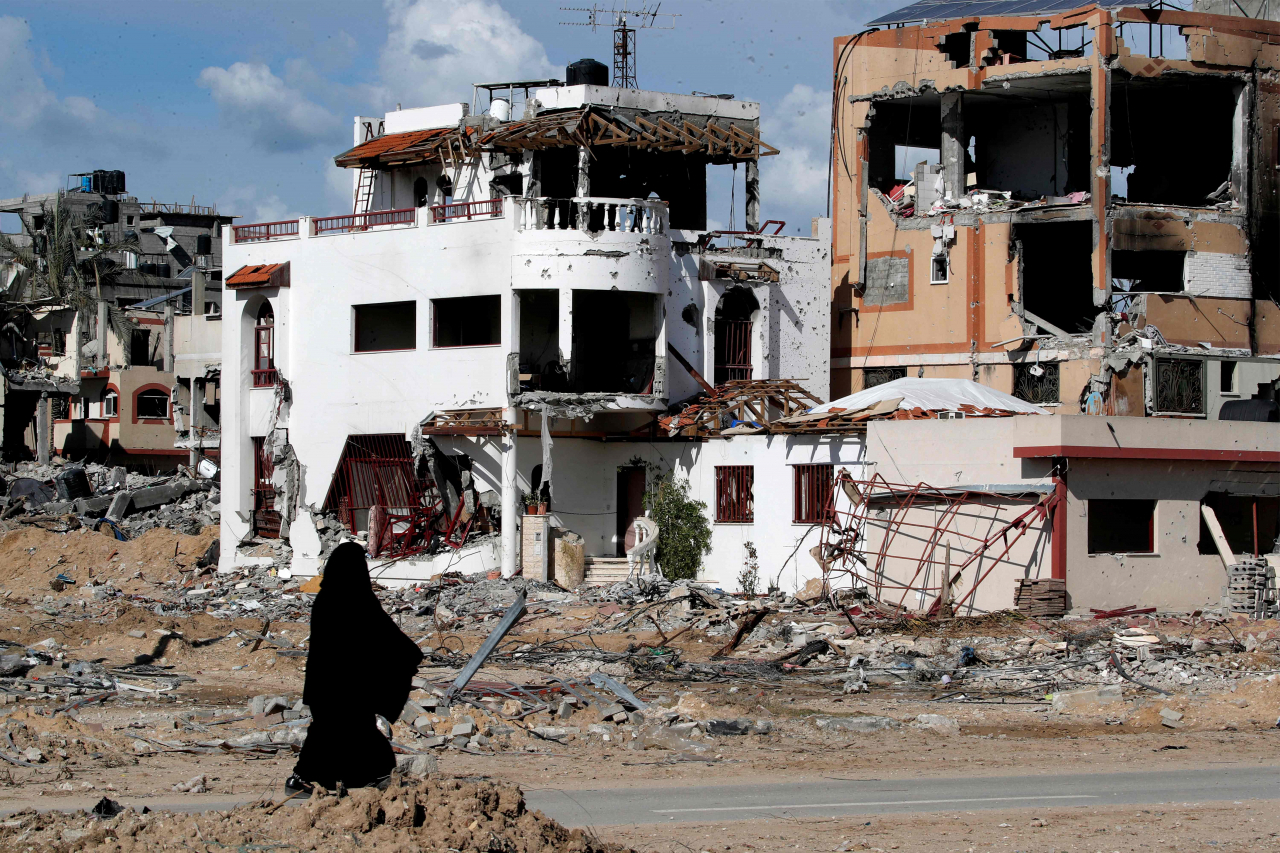 A woman walks past a destroyed building in the Maghazi camp for Palestinian refugees, which was severely damaged by Israeli bombardment amid the ongoing conflict in the Gaza Strip between Israel and the Palestinian militant group Hamas, in the central Gaza Strip on Thursday. (AFP)