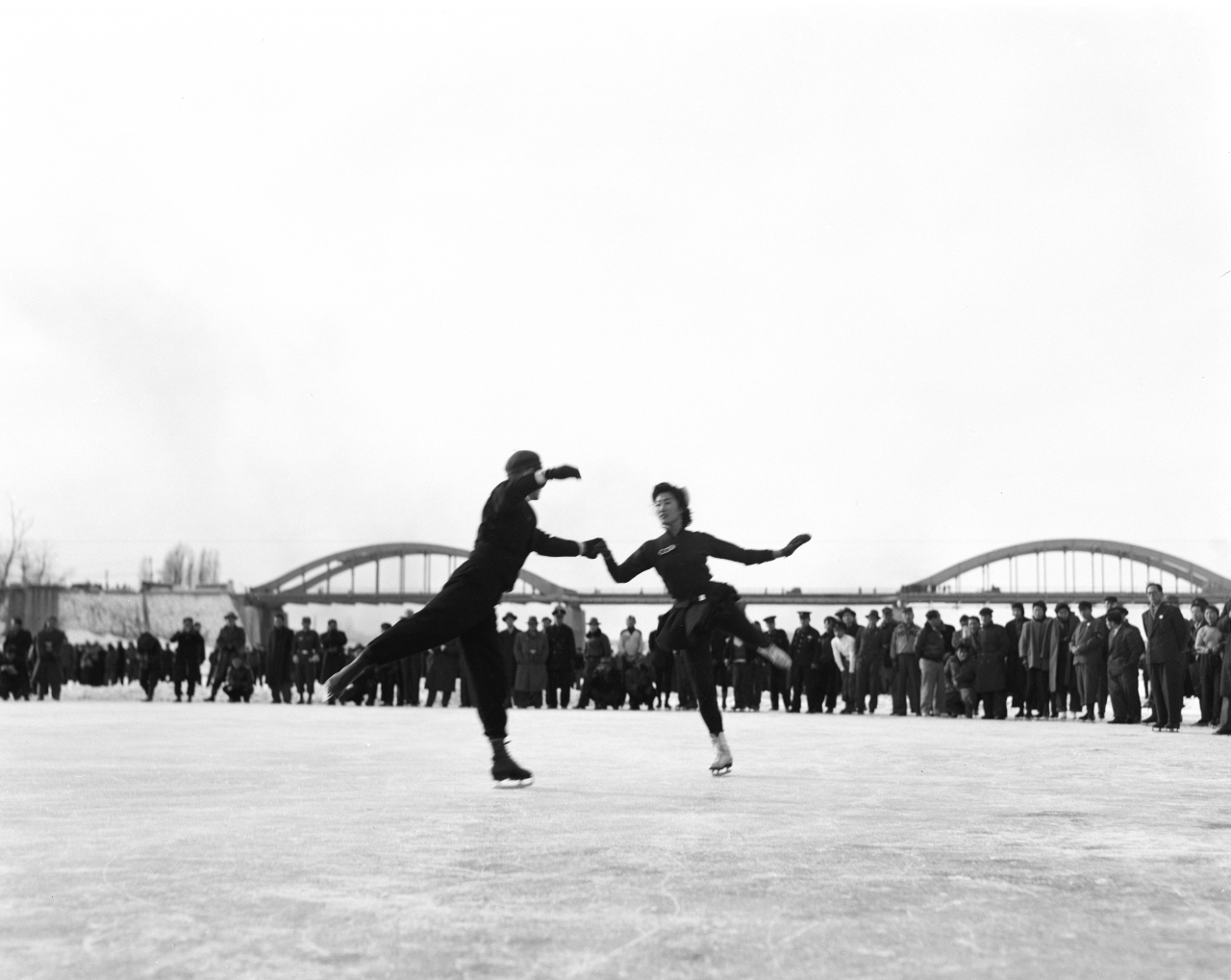 Figure skaters perform as a duo as spectators look on, during a 1956 winter sports event held in the middle of the frozen Han River. (National Archives of Korea)