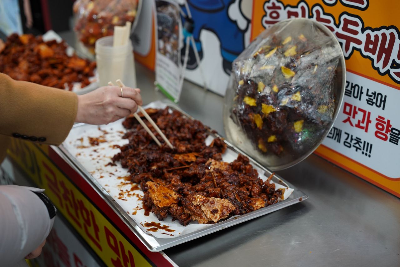 Diners try black garlic sweet crispy fried chicken at the Gugyeong Traditional Market in Danyang, North Chungcheong Province, Tuesday. (Lee Si-jin/The Korea Herald)