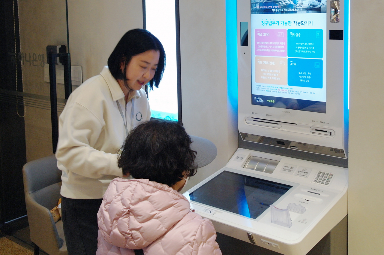 A Hana Bank employee (left) helps an old lady in using the ATM machine at the bank's branch in Tanhyeon-dong of Goyang in Gyeonggi Province. (Hana Bank)