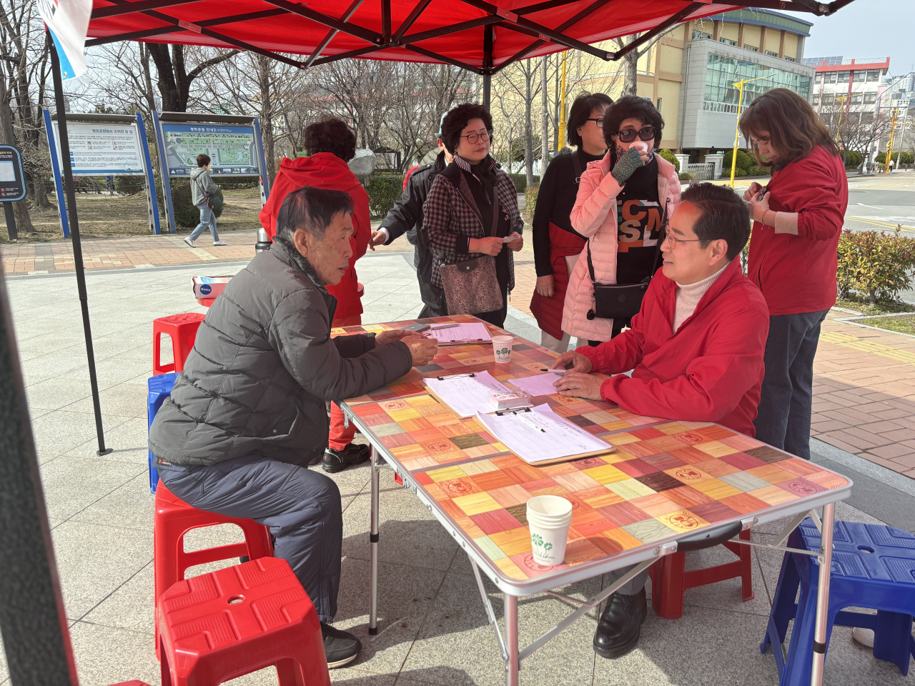 People Power Party Rep. Park Soo-young, sitting at the table in the red that represents his party, says he is setting up booths around the neighborhood every weekend to meet and hear out local residents in person. (Kim Arin/The Korea Herald)