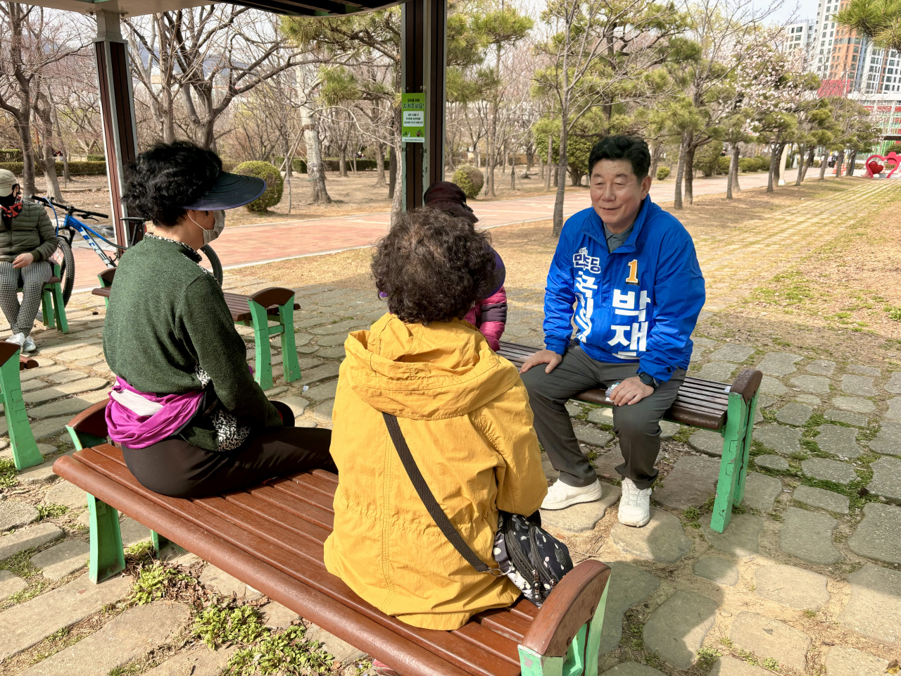 Democratic Party of Korea Rep. Park Jae-ho, clad in the blue that represents his party, speaks with residents at a park in Nam-gu, Busan, where he is running to be lawmaker, Sunday. (Kim Arin/The Korea Herald)