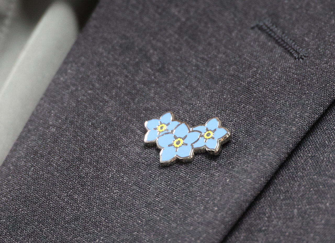 A symbolic forget-me-not badge is worn at the Unification Ministry on Wednesday. The emblem underscores the right to not be forgotten for abductees, detainees and prisoners of war in North Korea. (Yonhap)