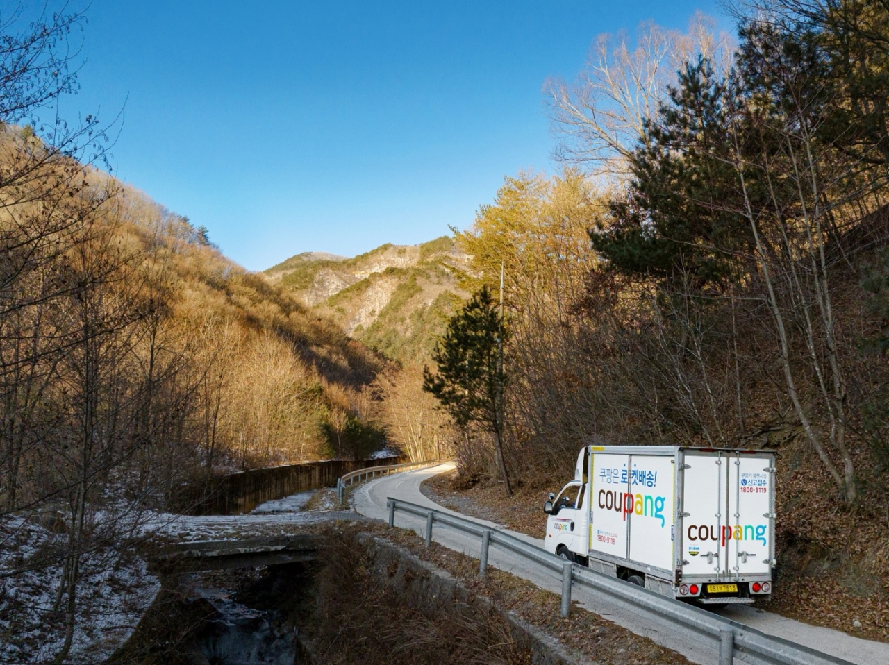 A Coupang delivery truck drives through a mountainous area. (Coupang)