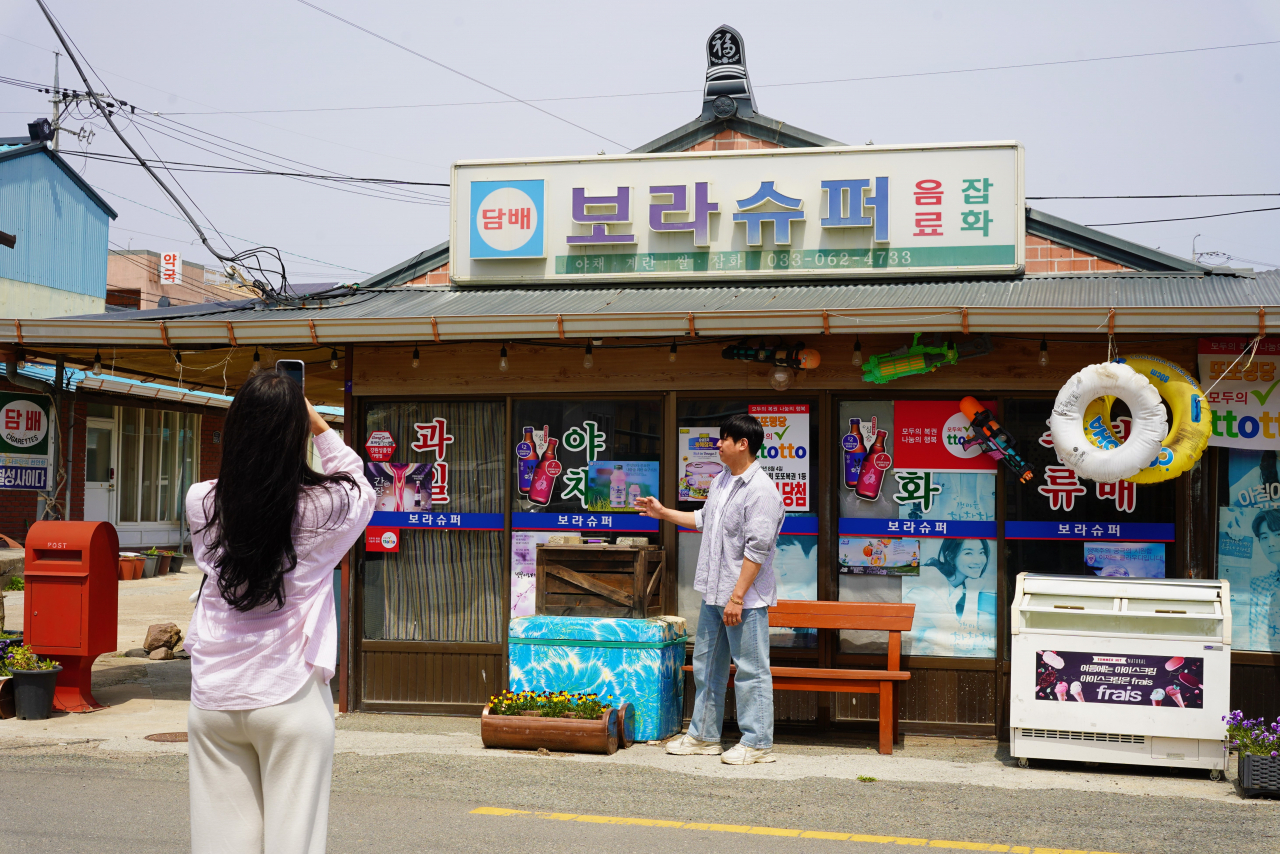 A visitor poses for a photo in front of Bora Supermarket at Cheongha Market in Pohang, North Gyeongsang Province, Wednesday. (Lee Si-jin/The Korea Herald)