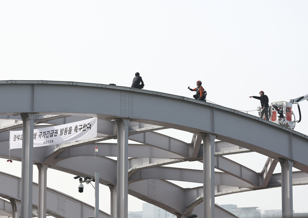 Rescue workers of Seoul talk to a man (left) who is protesting on the Hangangdaegyo bridge in Seoul on Wednesday. (Yonhap)