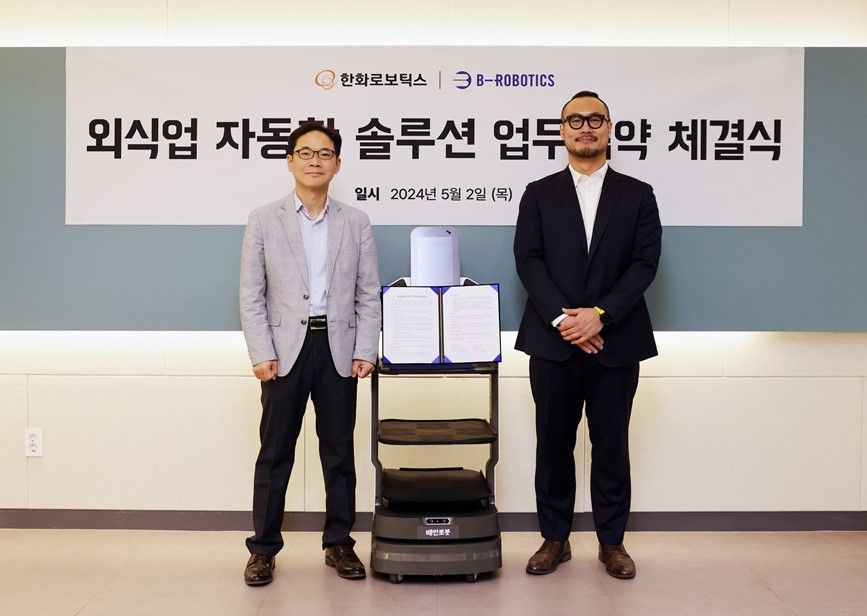 B-Robotics CEO Kim Min-soo (right) and Hanwha Robotics CEO Seo Jong-hwi pose for a photo, with the Baemin Robot S in the center, during a signing event on Thursday. (B-Robotics)