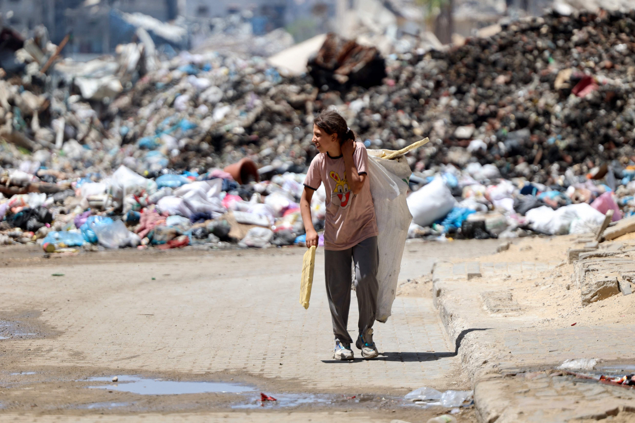 A Palestinian child transporting pieces of wood walks past a rubbish dump in Gaza City on Friday, amid the ongoing conflict between Israel and the militant group Hamas. (AFP)