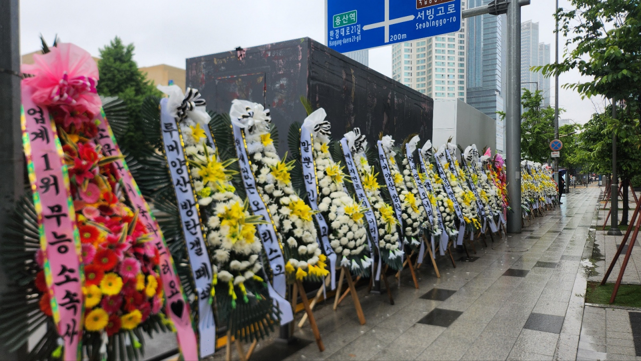 Flower wreaths with BTS fans' protesting messages against Hybe and Big Hit Music are displayed in front of Hybe's headquarters in Yongsan-gu, Seoul, Monday. (Lee Jung-youn/The Korea Herald)