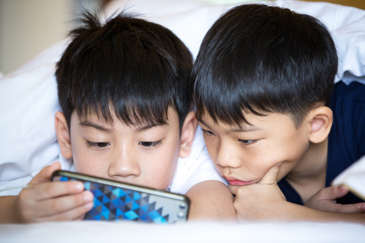 Two boys stare at a smartphone screen. (123rf)