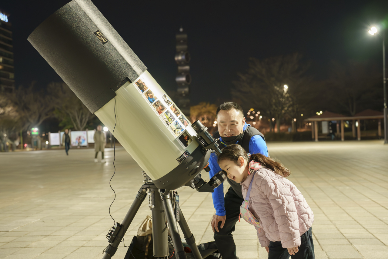 Hong Kee-cheon assists a girl in observing Jupiter through his telescope in a park in Ilsan, northwest of Seoul, in March. (Source: Hong Kee-cheon)
