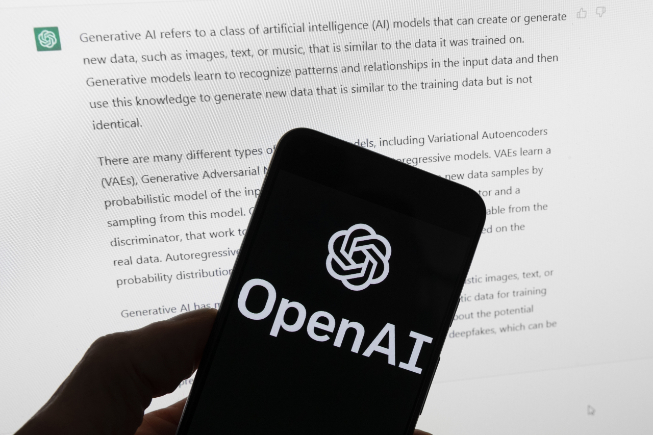 The OpenAI logo is seen on a mobile phone in front of a computer screen displaying output from ChatGPT in Boston on March 21, 2023. (AP-Yonhap)