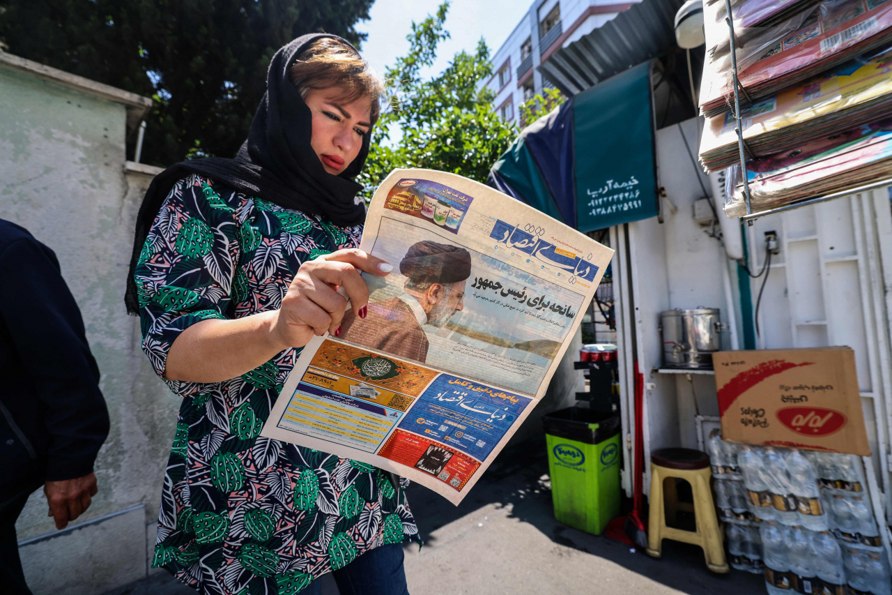 A woman reads a newspaper with a front-page report on the crash of the Iranian president's helicopter outside a kiosk in Tehran on Monday. (AFP-Yonhap)