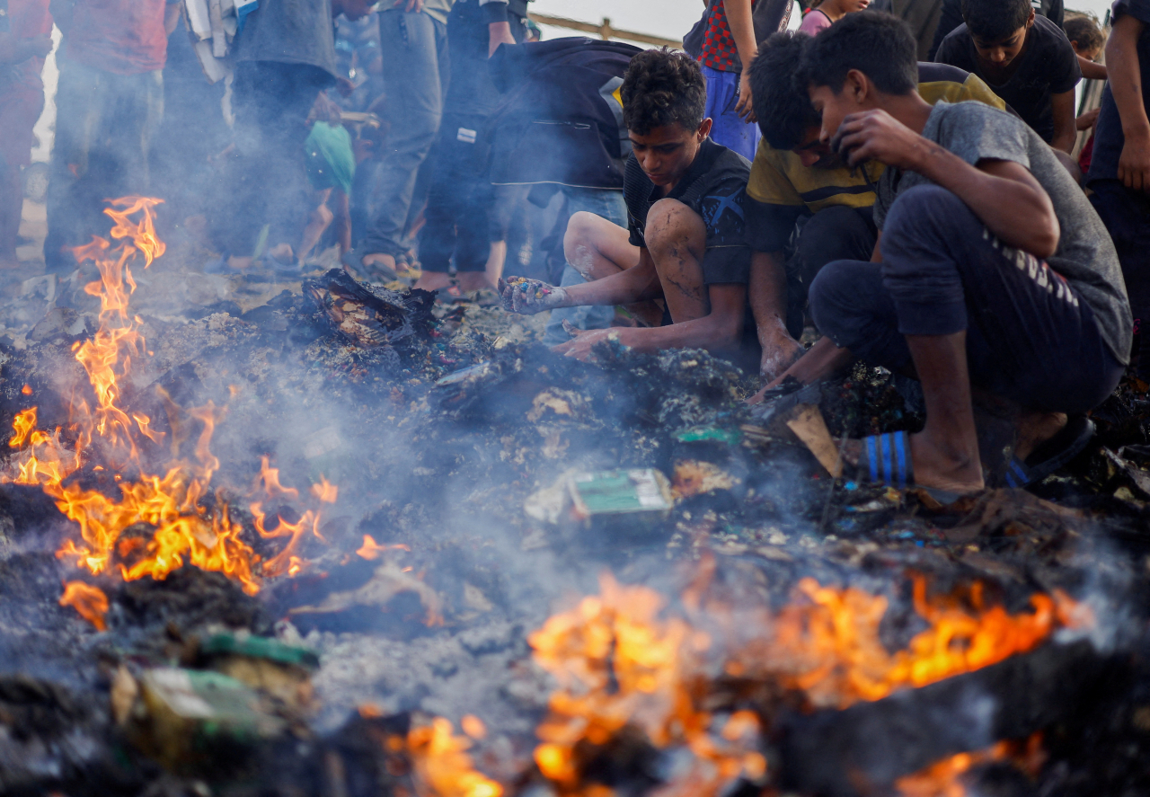 Palestinians search for food among burnt debris in the aftermath of an Israeli strike on an area designated for displaced people, in Rafah in the southern Gaza Strip, Monday. (Reuters-Yonhap)