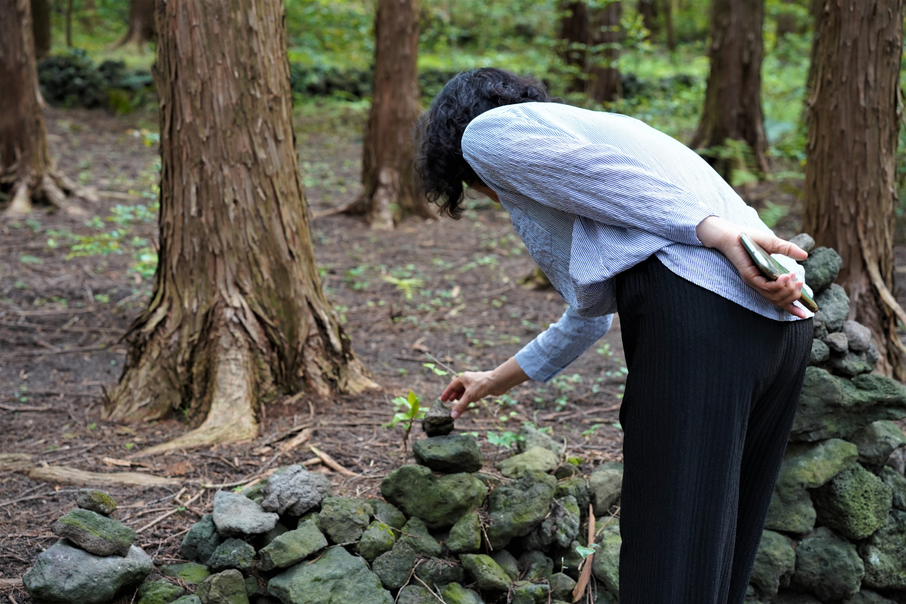 A visitor places a stone on a cairn in the cypress forest surrounding WE Hotel in Seogwipo, southern Jeju Island, May 22. (Lee Si-jin/The Korea Herald)