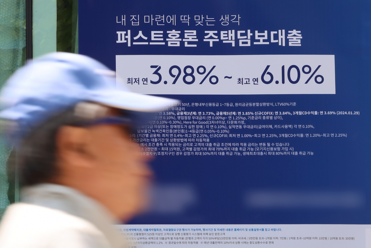 A man walks pass a sign about a bank's loan programs put up on the exterior of a lender in Seoul on May 9, 2024.
