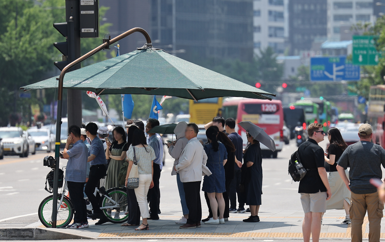 Pedestrians wait to cross the street under a giant parasol installed near a crosswalk in Jongno-gu, central Seoul, Wednesday. (Yonhap)