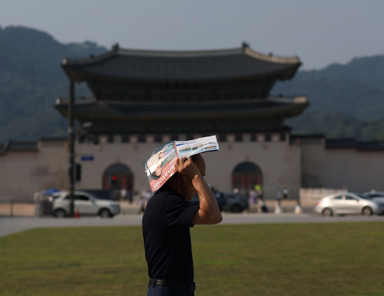 A pedestrian walks while covering his head with a pamphlet in the middle of a heat wave in Gwanghwamun Square, central Seoul, Wednesday. (Yonhap)
