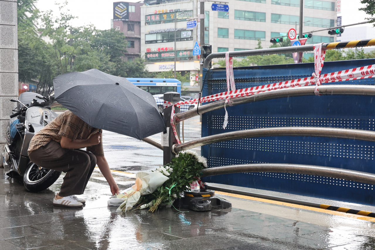 A pedestrian leaves a bouquet of chrysanthemums near Exit No. 7 of City Hall Station, Tuesday, the morning after a deadly car crash that resulted in nine casualties. (Yonhap)